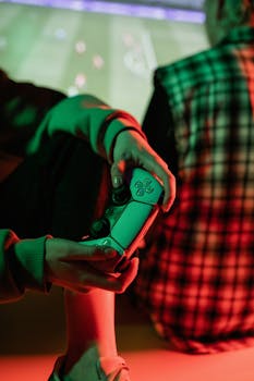 A gamer holds a video game controller in a warmly lit, cozy setting with a friend nearby.